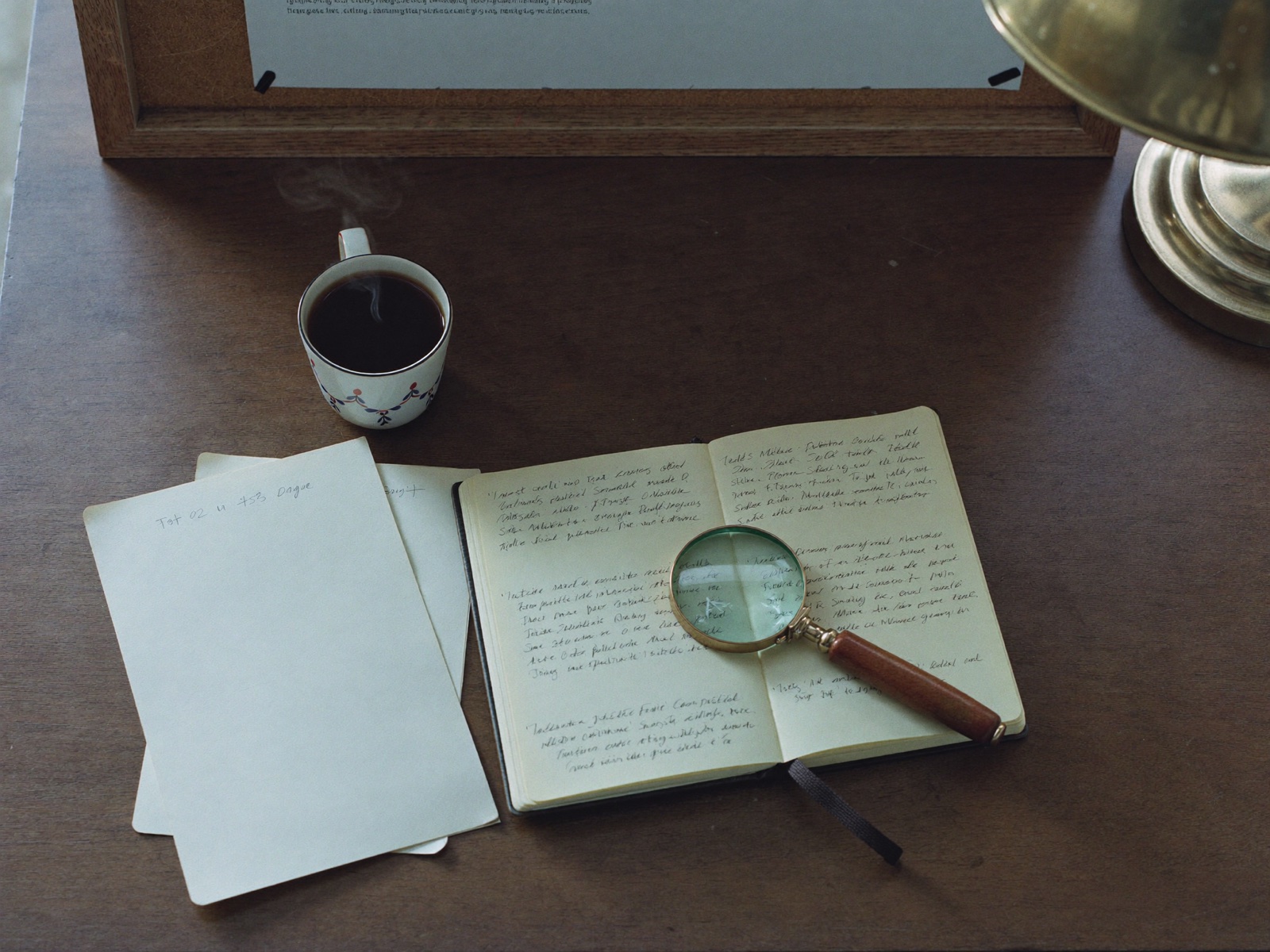 An investigator's desk with a loupe, notebook, and pinned research